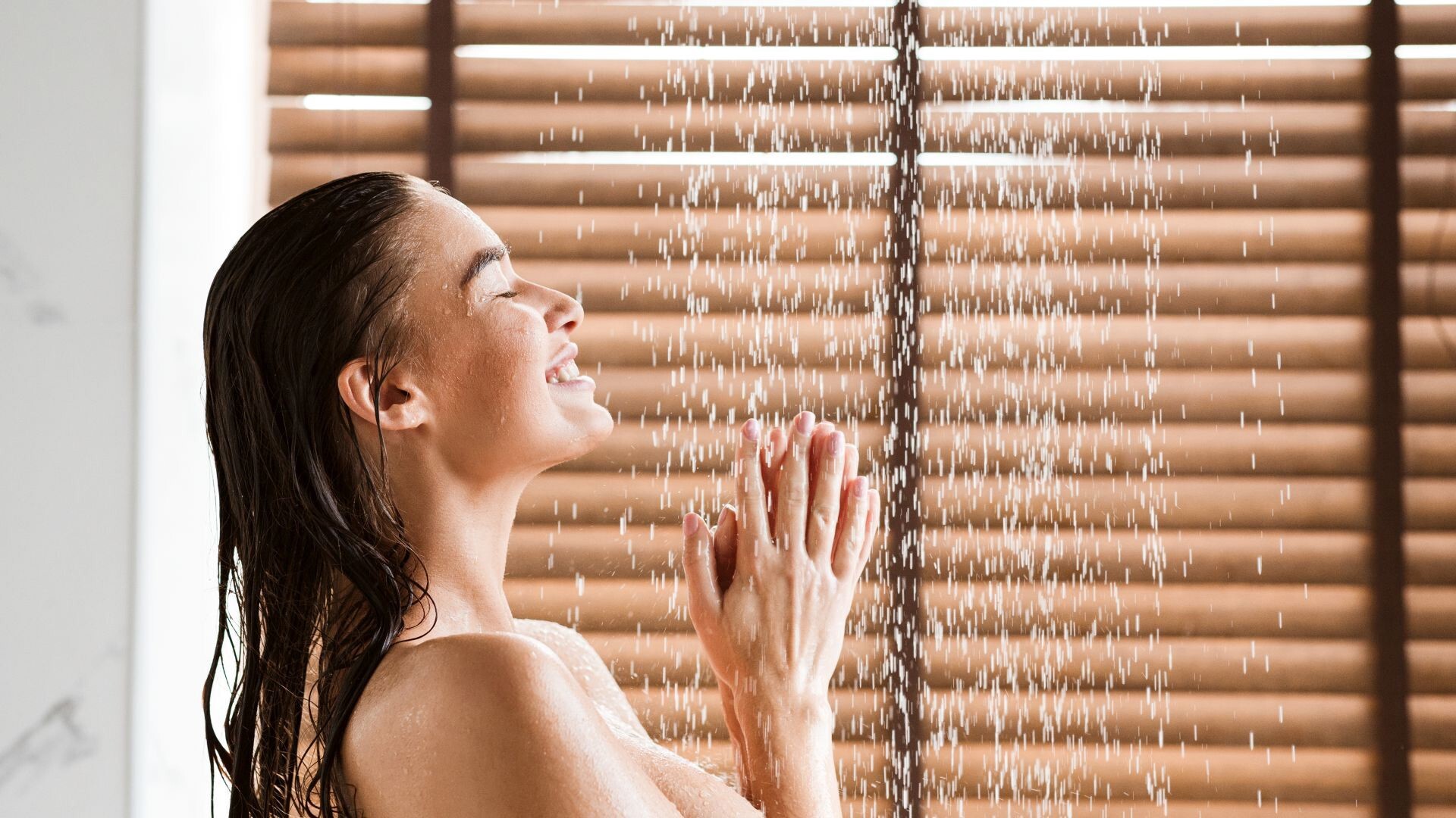 Frau genießt eine Dusche, lächelt und hält die Hände unter fließendes Wasser.
